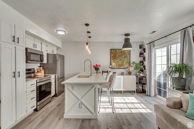 kitchen with appliances with stainless steel finishes, a sink, light wood-style floors, white cabinetry, and light countertops