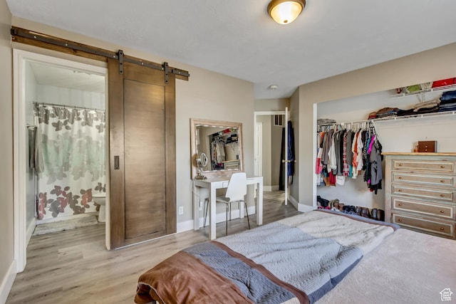 bedroom with a closet, wood finished floors, a barn door, and baseboards