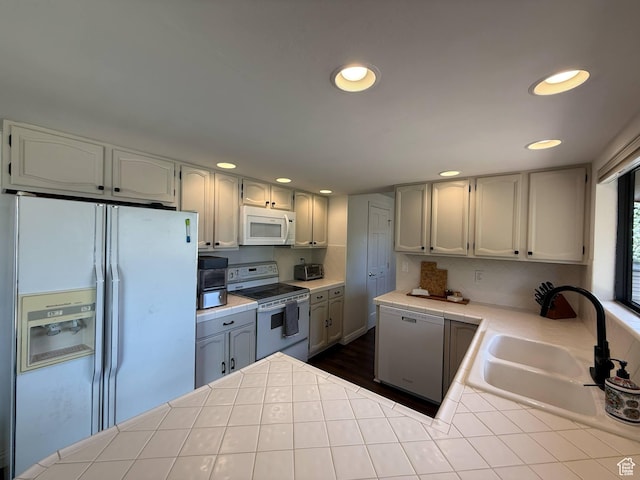 kitchen featuring white appliances, tile countertops, a sink, recessed lighting, and a peninsula