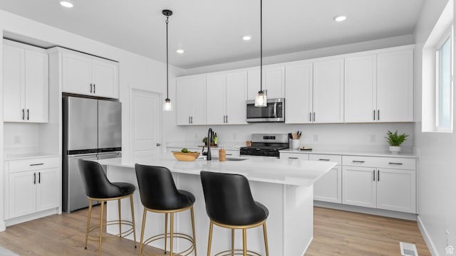 kitchen with appliances with stainless steel finishes, a sink, light countertops, a breakfast bar, and recessed lighting