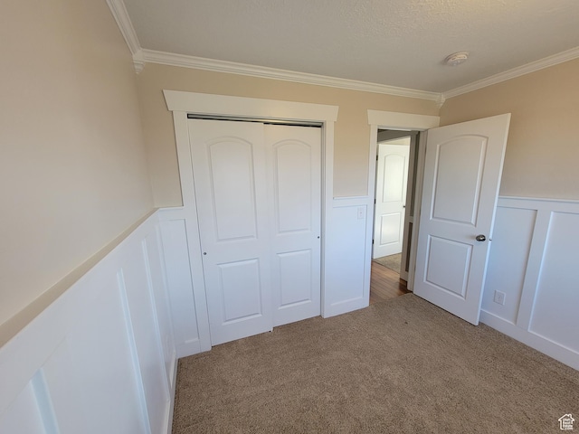 unfurnished bedroom featuring crown molding, a decorative wall, carpet, wainscoting, and a closet