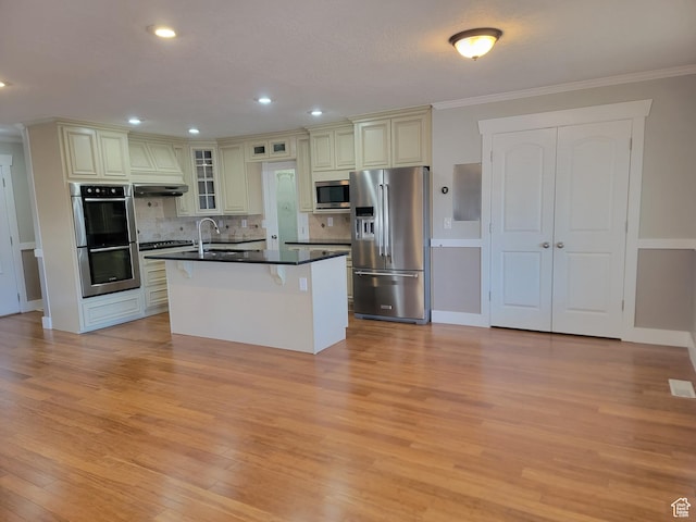 kitchen featuring stainless steel appliances, dark countertops, light wood-type flooring, cream cabinetry, and decorative backsplash