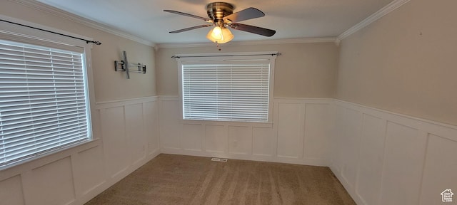 spare room featuring ceiling fan, wainscoting, crown molding, a decorative wall, and light colored carpet