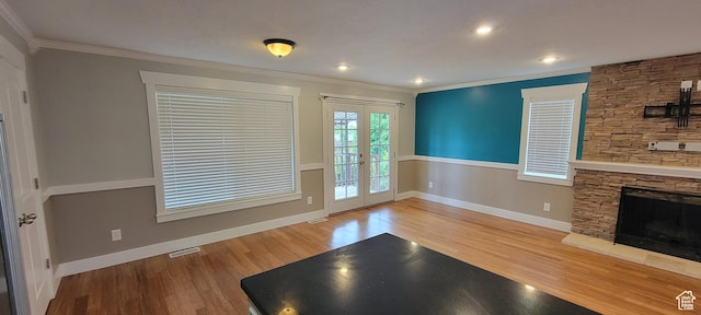 unfurnished living room with french doors, ornamental molding, wood finished floors, baseboards, and a stone fireplace
