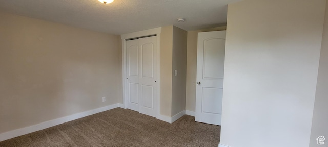 unfurnished bedroom featuring carpet flooring, baseboards, a closet, and a textured ceiling
