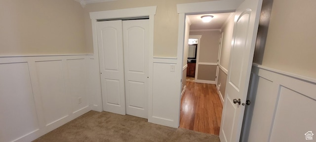 hall with crown molding, a decorative wall, and wainscoting
