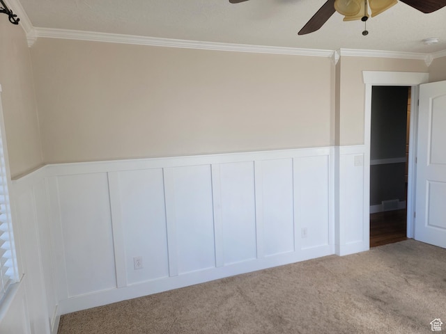 spare room featuring ceiling fan, a decorative wall, crown molding, carpet, and wainscoting
