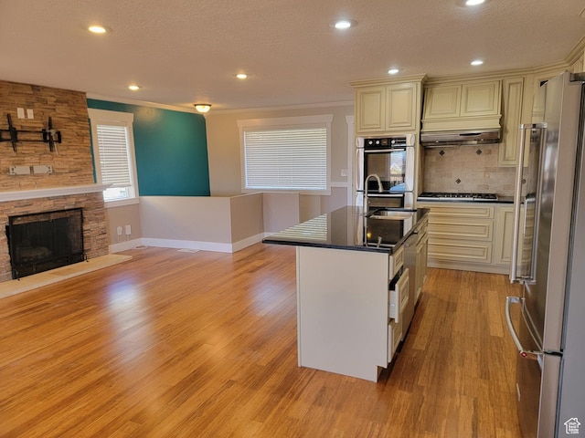kitchen featuring appliances with stainless steel finishes, a sink, dark countertops, light wood-style flooring, and cream cabinets