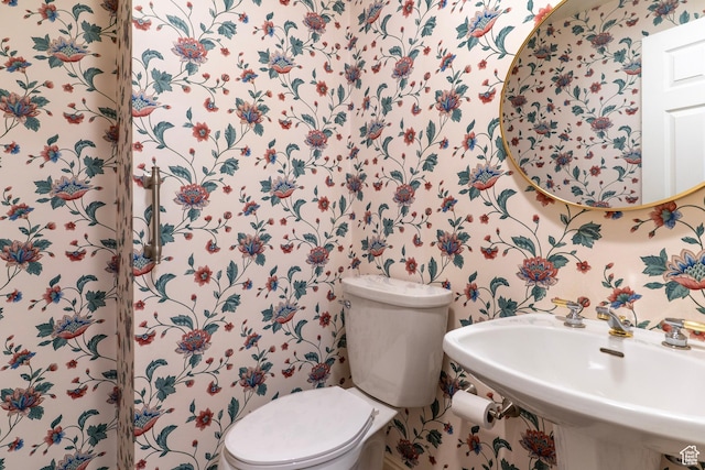 half bath featuring a sink, toilet, and wallpapered walls