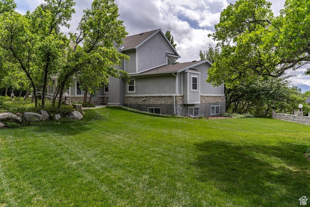 rear view of property with stucco siding, stone siding, and a yard