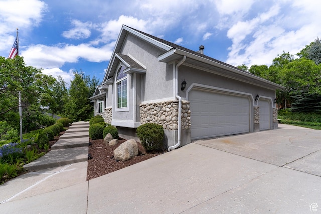 view of side of home featuring stucco siding, driveway, stone siding, and an attached garage