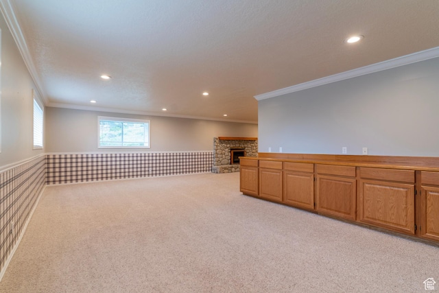 unfurnished room featuring crown molding, a wainscoted wall, light colored carpet, recessed lighting, and a stone fireplace