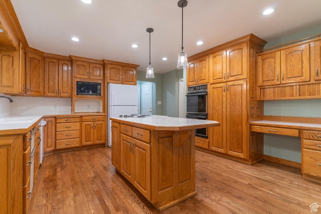 kitchen featuring black appliances, a sink, light wood finished floors, a center island, and recessed lighting