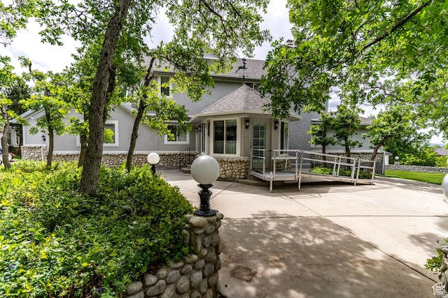 view of front facade with stucco siding, stone siding, a patio area, and roof with shingles