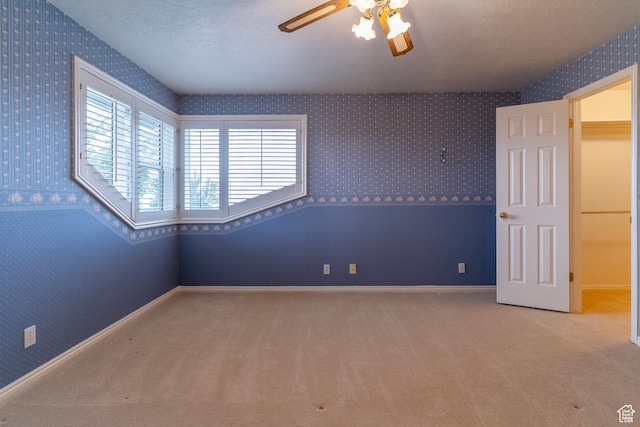 carpeted empty room featuring wallpapered walls, a ceiling fan, and baseboards