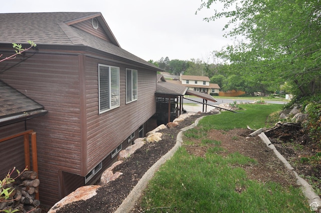 view of side of home featuring a shingled roof and a yard