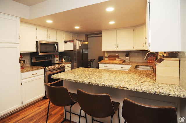kitchen with appliances with stainless steel finishes, a sink, a peninsula, white cabinetry, and recessed lighting