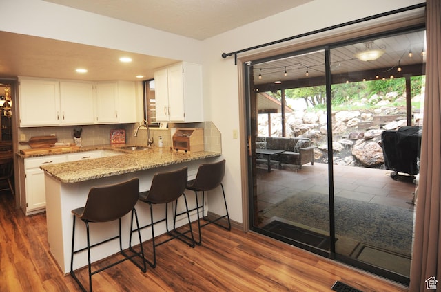 kitchen featuring a sink, white cabinets, backsplash, light stone counters, and recessed lighting