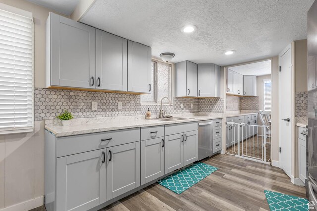 396 S 100 E, Tooele, UT 84074 - kitchen featuring stainless steel dishwasher, a sink, light wood-style floors, tasteful backsplash, and a textured ceiling