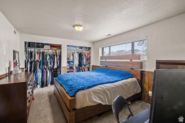 bedroom featuring two closets, a textured ceiling, and carpet floors