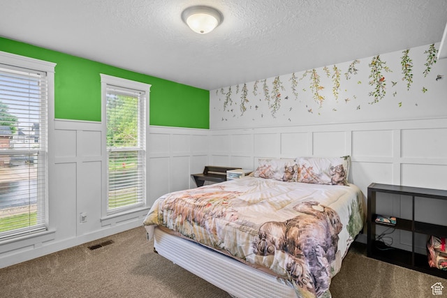 bedroom featuring a decorative wall, wainscoting, a textured ceiling, and carpet