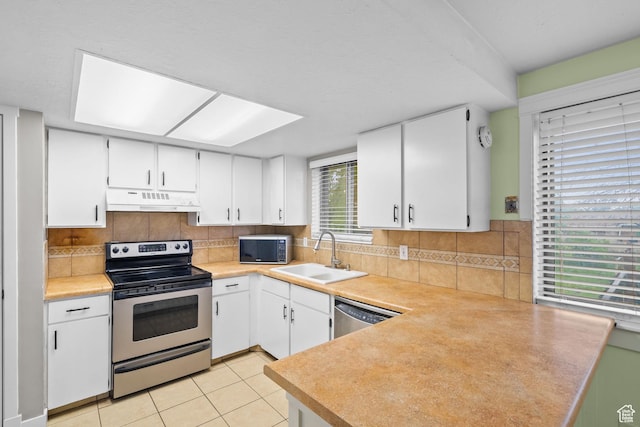 kitchen with stainless steel appliances, a sink, under cabinet range hood, a peninsula, and white cabinets