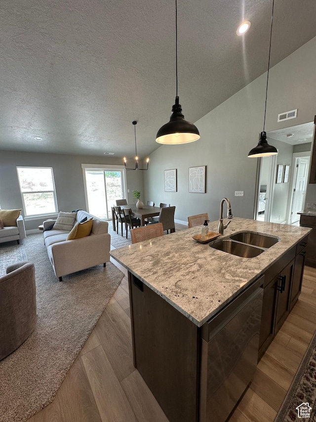 kitchen with a sink, light wood-type flooring, open floor plan, a textured ceiling, and a center island with sink