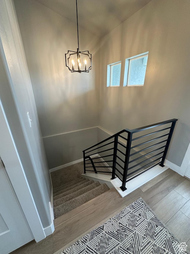 stairway with a chandelier, wood finished floors, and baseboards