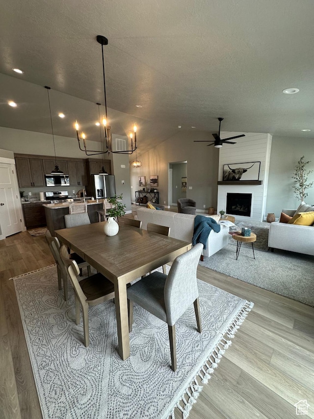 dining space with wood finished floors, recessed lighting, a chandelier, a large fireplace, and a ceiling fan