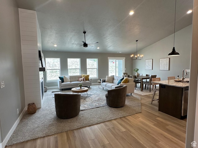 living room with wood finished floors, a ceiling fan, a chandelier, baseboards, and lofted ceiling