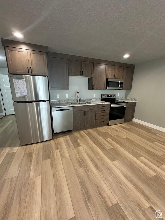 kitchen with appliances with stainless steel finishes, a sink, a textured ceiling, light wood-style floors, and baseboards