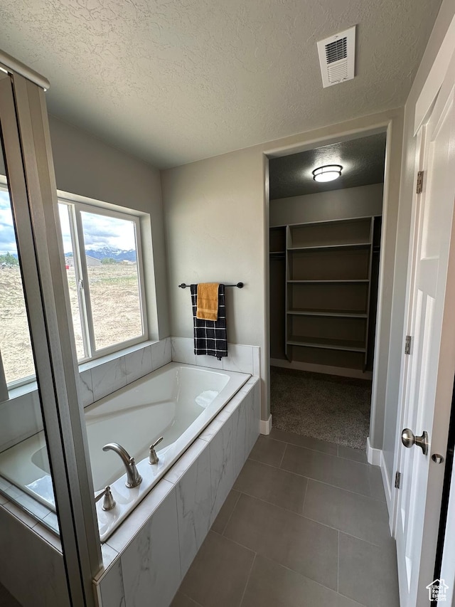 bathroom featuring a textured ceiling, a walk in closet, a garden tub, tile patterned flooring, and baseboards