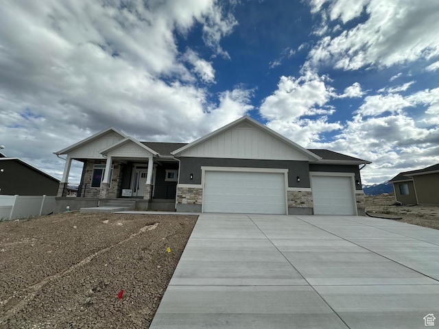 craftsman inspired home featuring stone siding, an attached garage, covered porch, concrete driveway, and fence