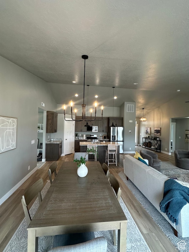 dining space featuring lofted ceiling, dark wood-style floors, a chandelier, baseboards, and a textured ceiling