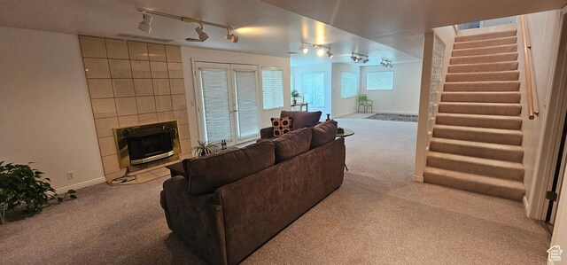 living room with carpet floors, track lighting, stairs, and a tile fireplace
