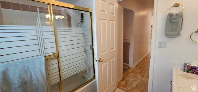 bathroom featuring wood finished floors and combined bath / shower with glass door