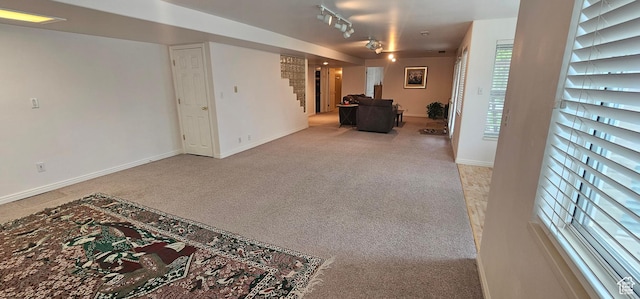 carpeted living area featuring baseboards, stairway, and track lighting