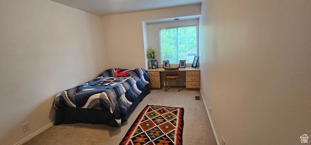 bedroom with light carpet, an office area, and baseboards