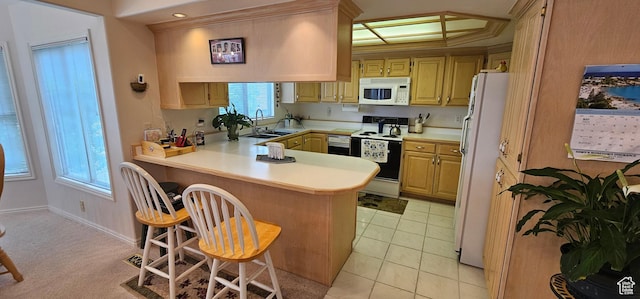 kitchen featuring white appliances, a peninsula, light countertops, a sink, and a kitchen bar