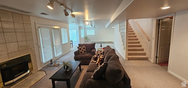 carpeted living room with rail lighting, a tile fireplace, stairs, and baseboards