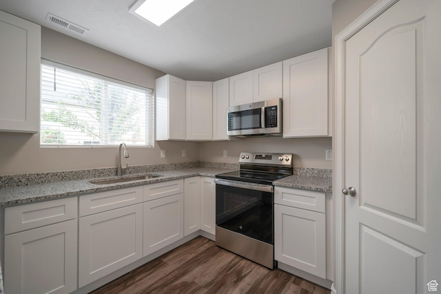 kitchen with stainless steel appliances, a sink, dark wood-style flooring, and white cabinets