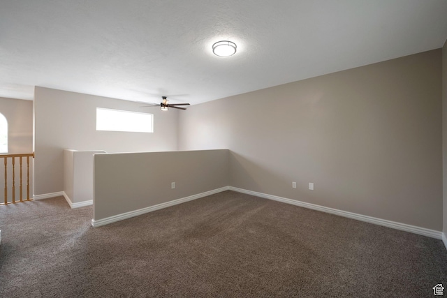 spare room featuring dark colored carpet, a ceiling fan, and baseboards