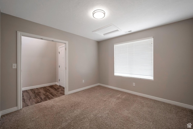empty room featuring carpet flooring, attic access, and baseboards