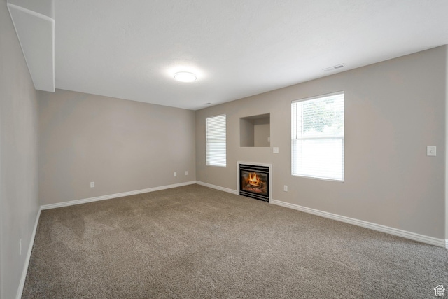 unfurnished living room featuring carpet floors, baseboards, and a glass covered fireplace