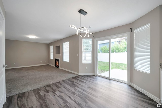 empty room featuring wood finished floors, baseboards, a glass covered fireplace, and a chandelier