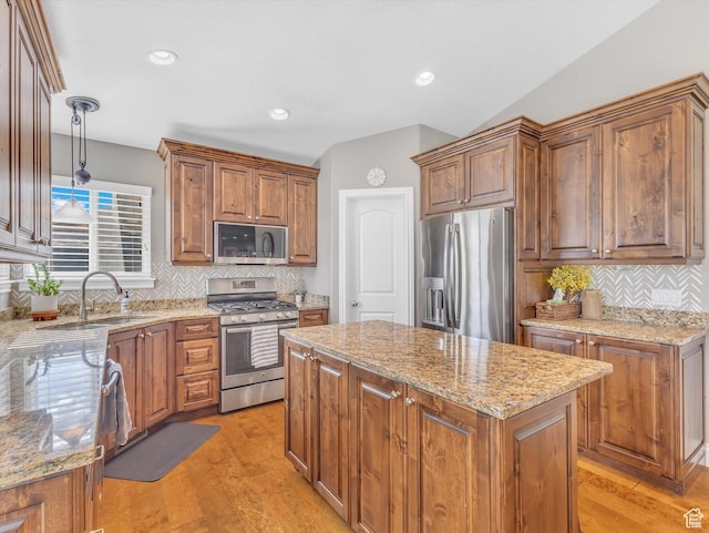kitchen with appliances with stainless steel finishes, a sink, a center island, light stone countertops, and tasteful backsplash
