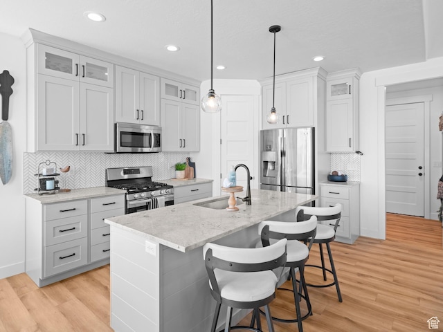kitchen featuring appliances with stainless steel finishes, a sink, an island with sink, light wood-style flooring, and recessed lighting