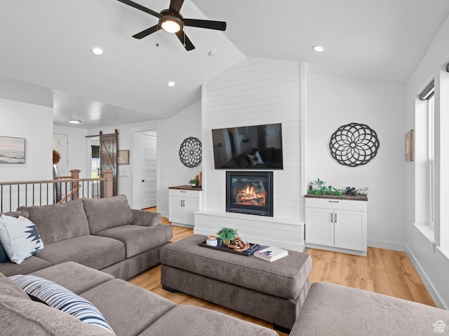 living area featuring a barn door, ceiling fan, light wood-style floors, lofted ceiling, and a fireplace