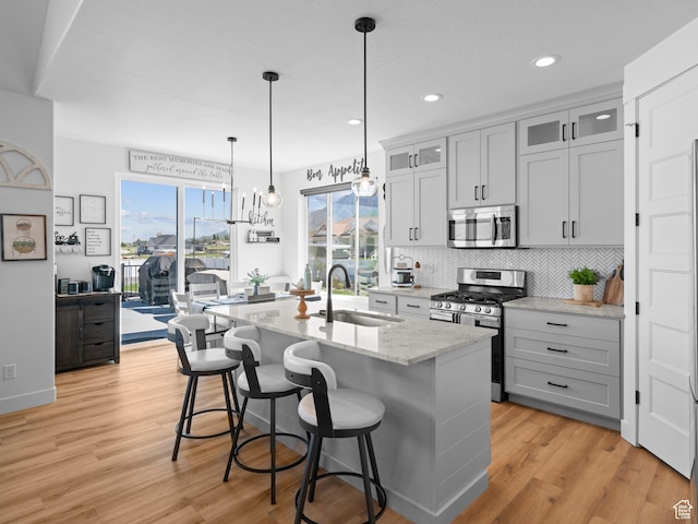 kitchen with appliances with stainless steel finishes, a sink, a kitchen island with sink, light wood-style floors, and recessed lighting