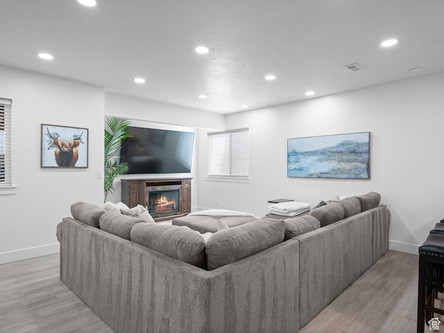 living room featuring recessed lighting, baseboards, light wood finished floors, and a glass covered fireplace
